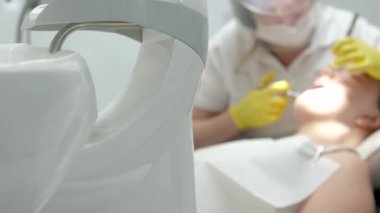 Diş hekimliği ergenliği, sarı eldivenli bir doktor dişçide dişçiye yakın çekim videosu için genç bir kızın dişini doldurur ve dişini yeni teknolojilerle kurutur. modern klinik