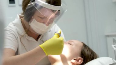 Diş hekimliği ergenliği, sarı eldivenli bir doktor dişçide dişçiye yakın çekim videosu için genç bir kızın dişini doldurur ve dişini yeni teknolojilerle kurutur. modern klinik