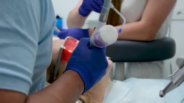 Bir diş kliniğinde diş temizliği, taş ve plaket çıkarmak, bir kadınla çalışan genç uzmanlar, salya püskürtücüsünü temizlemek, tükürük emmek, dişlere boya sürmek,