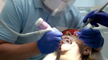 Bir diş kliniğinde diş temizliği, taş ve plaket çıkarmak, bir kadınla çalışan genç uzmanlar, salya püskürtücüsünü temizlemek, tükürük emmek, dişlere boya sürmek,