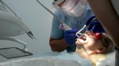Bir diş kliniğinde diş temizliği, taş ve plaket çıkarmak, bir kadınla çalışan genç uzmanlar, salya püskürtücüsünü temizlemek, tükürük emmek, dişlere boya sürmek,