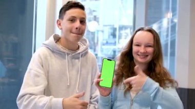 Gülümseyen kızıl uzun saçlı genç çocuk yeşil ekran krom anahtarı ile yatay telefon gösteriyor ve evde konuşmalar, ürün sunumu, gençlik uygulaması, oyun ve çevrimiçi dükkan reklamcılığı. Yüksek kalite 4k