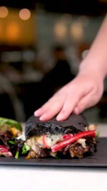 Lezzetli sandviçe siyah çörekle bir sürü biber peynirli et salatası yakın plan kadın eli sıkan hamburger, ısırılan lezzetli yiyecek ve kontrol kalitesi. Tadını