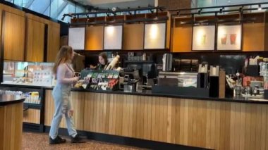 Starbucks 'ta vakit geçiren genç bir kız Machalata satın alıyor fotoğraf çekiyor Wi-fi içiyor güzel zaman geçiriyor kot pantolon, leylak rengi ahşap iç mekan Kanada Vancouver 09.09.2023