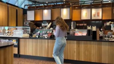 Starbucks 'ta vakit geçiren genç bir kız Machalata satın alıyor fotoğraf çekiyor Wi-fi içiyor güzel zaman geçiriyor kot pantolon, leylak rengi ahşap iç mekan Kanada Vancouver 09.09.2023