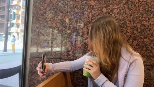 カフェでスターバックスの若い女の子がマカラタを買って写真を撮ったとき ジーンズライラックブラウス木製の内装カナダバンクーバーを飲みながらWifiを飲みました 2023 — ストック動画