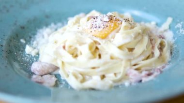 Restoranda Carbonara usulü yumurta sarısı servis ediliyor. Tabağın ortasında bıçak ve çatal ile kesilmiş yumurta sarısı var. Mavi benekli domuz pastırması servis ediliyor. parmesan peyniri