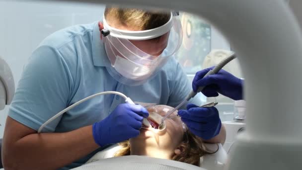 最新の技術クリーニングとホワイトニング歯科看護師と若い女性患者ティーンエイジャーマスクの歯を治療する医師は清潔な衛生を手袋します クリニックの歯科オフィスで最新のデバイス — ストック動画