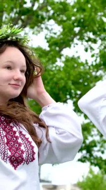 Güzel genç kadınlar çelenk dokuyorlar gülüyorlar bahçede çene çalıyorlar ulusal Ukrayna gömlekleri nakışlıyorlar ayçiçeği çiçekleri ve orman beyazından çelenkler. 