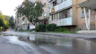 Vinnitsa, Ukrayna 'da sıradan bir avlu, beş katlı bir panelhane, boru patladı, sıcak su asfalta akıyor, kaldırıma dökülüyor, arabalar, ağaçlar, iç huzuru.