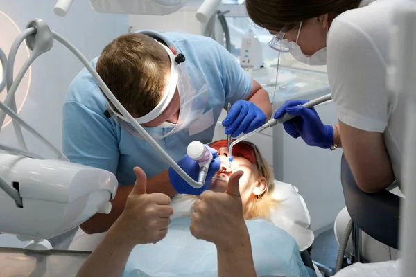 professional teeth cleaning in a dental clinic, removing stones and plaque, young specialists working with a woman, cleaning a saliva ejector, sucking out saliva, applying paint to the teeth