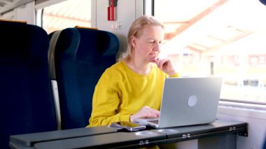 Trende oturan bir kadın masadaki dizüstü bilgisayarda çalışıyor orta yaşlı bir kadın reklam amaçlı dizüstü bilgisayarlı gülme alanı gösteren bir telefonun reklamını yapıyor.