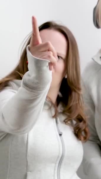 男的和女的两个少女用食指做着消极的摆动不 不要这样做 不要看那只手伸向镜框 用食指前置耳机的运动服 白色背景 — 图库视频影像