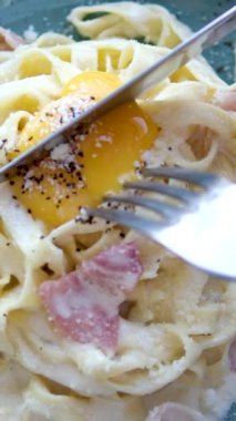 Restoranda Carbonara usulü yumurta sarısı servis ediliyor. Tabağın ortasında bıçak ve çatal ile kesilmiş yumurta sarısı var. Mavi benekli domuz pastırması servis ediliyor. parmesan peyniri