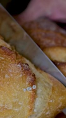 Tam tahıllı ekmek mutfak ahşap tabağına konmuş ve şefin elinde altın bıçak var. Masanın üzerinde taze ekmek var. Mutfak masasında taze ekmek sağlıklı beslenme ve geleneksel fırın konsepti