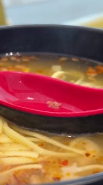 Domuz eti ve karidesli erişte çorbası Asya mutfağı sıcak vermicelli çorbası ve siyah kase. Kırmızı oryantal kaşıkla buharlı yemek sağlıklı öğle yemeği Koreliler, Tayvan Vietnamlılar doğru dürüst yemek yer.