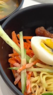 Tayvan usulü kuru erişte yarı haşlanmış yumurta, Tayvan mutfağı siyah tabakta Asya yemeği. Haşlanmış vermicelli yemek çubuklarıyla. Sebzelerin altında salatalık havucu ve jülyen gibi sağlıklı.