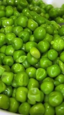 Tabakta yeşil bezelyeler var, bir kısmı kaşık kaşık kazanıyor. Yüksek kalite 4k görüntü