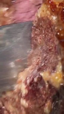 bbq, kebap büyük bir parça sulu eti büyük bir bıçakla kesti. Küçük demir spatula yağıyla tabaktan çıkarıyorlar. Kan akıyor.