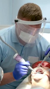 Bir diş kliniğinde diş temizliği, taş ve plaket çıkarmak, bir kadınla çalışan genç uzmanlar, salya püskürtücüsünü temizlemek, tükürük emmek, dişlere boya sürmek,