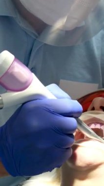 Bir diş kliniğinde diş temizliği, taş ve plaket çıkarmak, bir kadınla çalışan genç uzmanlar, salya püskürtücüsünü temizlemek, tükürük emmek, dişlere boya sürmek,