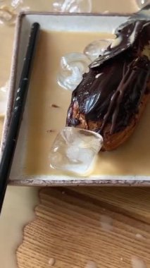 Ahşap bir masada bir bardak kırıldı, kapuçino latte kahve döküldü, bir tabak cam kırığı ve yanında bir kamışla birlikte bir tabak pasta döküldü, rahatsız edici bir kahve döküldü. Restoranda temizlik.