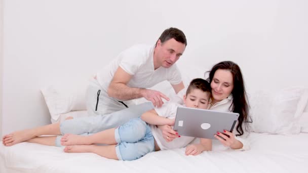 2007 13阅读 最新科技新婚夫妇和孩子坐在笔记本电脑上看电影 一起在床上放松自己 穿上白色的衣服 — 图库视频影像