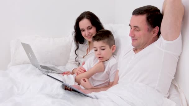 2007 13阅读 最新科技新婚夫妇和孩子坐在笔记本电脑上看电影 一起在床上放松自己 穿上白色的衣服 — 图库视频影像