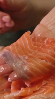 Keskin bıçakla büyük kırmızı balık parçalarını kestiler. Ağır çekim suşi için tuzlanmış somon balığı pişirdiler.