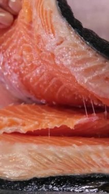 Eller yakın çekim pişirir. Şef bıçakla keser, kırmızı balık, tahta kesme tahtasına somon füme. Arkaplanda siyah ahşap masa.