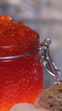 Arka planda kırmızı havyar olan teneke kutuyu aç. El bir kaşık tutuyor ve kırmızı havyarı kavanozdan çıkarıyor. Yüksek kalite 4k görüntü