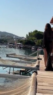 Arnavutluk 'ta VIP deniz kenarı tatili. Siyah pareo yürüyüşlü bir kadının hamağı üzerinde. Yavaş çekim videosu telefonun elinde. Harika bir hobi, rahatla. Güneş yatağının üzerinde beyaz pireler boyunca yürü.