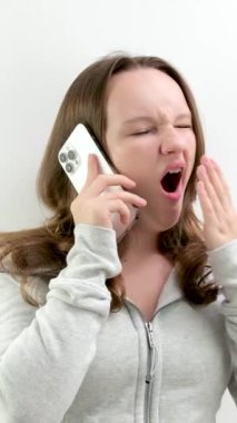 Telefonda esnerken tatsız, sıkıcı bir sohbet sırasında genç bir kız ağzını el esnemeleriyle kapatıyor. Stüdyoda dinlenmekten bıkmış bir genç kız. beyaz telefon tatmin olmamış kupada yüzünü büküyor