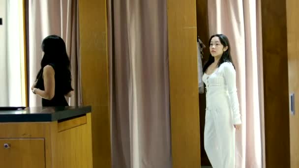 两个亚洲女孩试穿衣服 黑色的 白色的 更衣室里的选择商店里买正装的衣服直发经典昂贵的部门价格标签看看镜子阿丽夏温哥华 — 图库视频影像