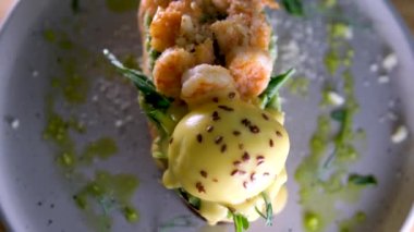Lezzetli karides karidesli Benedict peynirli avokado ve yumurtalı tost. Parmesan yeşili iştah açıcı aromatik öğle yemeği aperatifi. Gri tabakta keten taneleri serpiştirilmiş. Restoran servisi