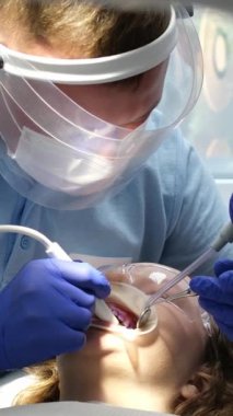 En son teknoloji temizliği ve diş beyazlatma hemşiresi ve doktor genç bir dişçinin dişlerini tedavi ediyor. Genç bir kızın maskeleri eldivenleri temizleme temizliği yapıyor. Klinikteki en son cihaz.