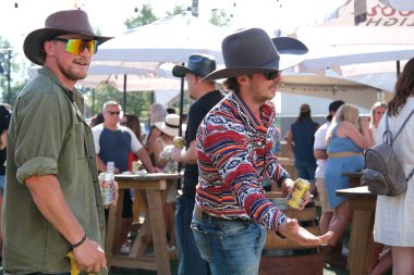 Vancouver 'da izinli insanlar içki alırlar salıncaklara binerler kovboy şapkaları giyerler parkta yürürler Surrey Kanada şehrinde gerçek insanlar 05.20.2023