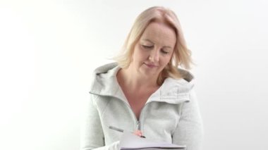 Gelecek için planlar yapan, kalemle bir not defterine yazan, beyaz arkaplanlı yetişkin sarışın bir kadın satın alma günü için fikir planları yazan, düşünmesi gereken kararlar veren. Başını kaldır.