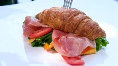 Beyaz tabağa konmuş jambon ve peynirli lezzetli kruvasan. Prosciutto ve otlu kruvasan çatalla batıyor ve bıçakla kesiliyor.