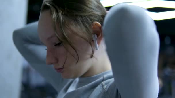 灰色のトラックスーツジムの若い女の子 ダークジムで ヘッドフォン エクササイズ 体の世話 飲料水 ビデオセット スリムボディ ハッピーワークアウト カーディオ — ストック動画