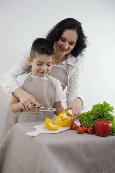 cooking courses for children mom teaches to cut vegetables with knife yellow bell pepper finely chopped into strips in family at home white background apron kitchen vegetables lettuce leaves
