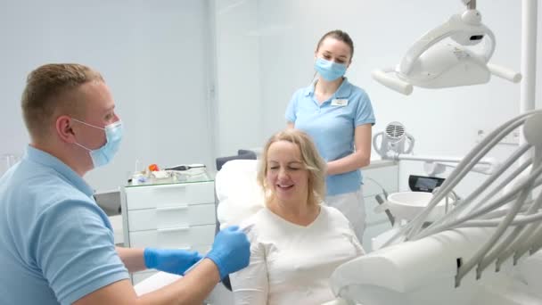 歯の色を決定するための古典的な歯科着色歯科医院の医師の手ミラー上中年女性患者彼女は結果の笑顔で満足している彼女は親指を示しています笑うと鏡を与えます — ストック動画