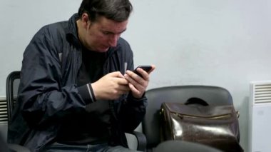 Yüzünde sivilceler, cilt problemleri, telefonda konuşma, eski evrak çantası sandalyede, öğretmen, muhasebeci, fakir, siyah ceket, çekingenlik, elleriyle başını kaşıma. Yıkanmamış saç