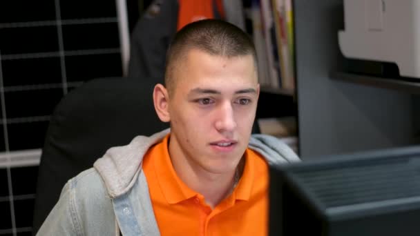 仕事のオンライン調査 オフィスのオフィスでインターネット配信マネージャーのオレンジ色の明るいシャツの灰色のパーカーの若者を検索します 仕事練習 ショートヘアライト — ストック動画