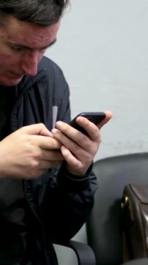 Yüzünde sivilceler, cilt problemleri, telefonda konuşma, eski evrak çantası sandalyede, öğretmen, muhasebeci, fakir, siyah ceket, çekingenlik, elleriyle başını kaşıma. Yıkanmamış saç