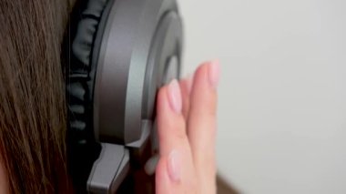close-up fingers drumming on large professional earpiece Girl listening to music tapping fingers to beat on ear close-up space for text musicality teach music lesson white background womans ear