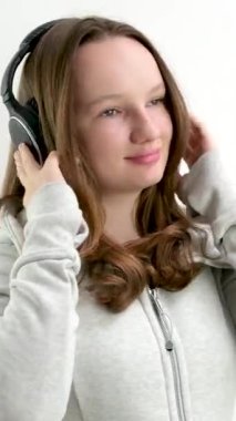 Genç kız büyük profesyonel kulaklıklarla müzik dinliyor beyaz arka planda spor bir takım elbise giymiş güzel bir ergen gibi gülümsüyor. ergenlik