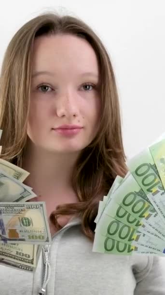 金发碧眼的少女 两大包新钞票 100美元钞票 100欧元钞票 白色背景 身穿灰色运动衫 蓬松的头发 年轻自信的女孩 新一代 — 图库视频影像