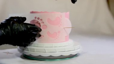 Çocuk dekorasyonu için doğum günü pastası hazırlıyorum şablona pembe krem sürüyorum çocuk dekorasyonu profesyonel pasta dükkanı Christina 'nın 1 yaşındaki bebeğinin bacakları şeklinde. siyah eldivenler