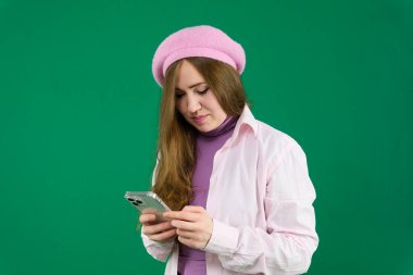 Kafasında pembe bereli genç bir kadın yeşil arka plan kromatonunda Fransa modası. farklı duygular pembe ceket eldivenler uzun kahverengi saçlar